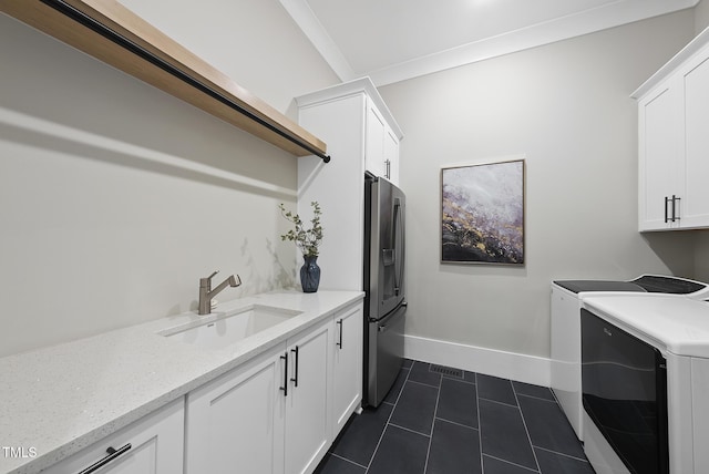 clothes washing area with washer and clothes dryer, a sink, baseboards, cabinet space, and dark tile patterned floors