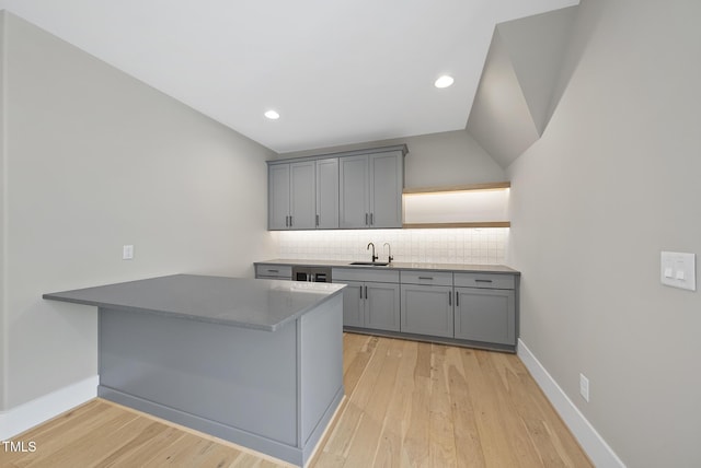 kitchen featuring light wood finished floors, gray cabinets, a sink, a peninsula, and tasteful backsplash