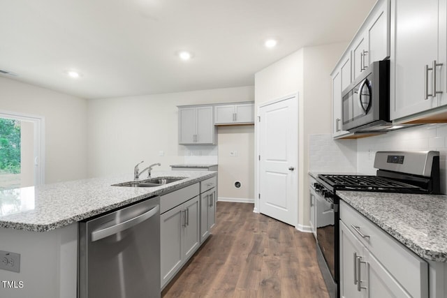 kitchen featuring appliances with stainless steel finishes, sink, backsplash, light stone counters, and a center island with sink