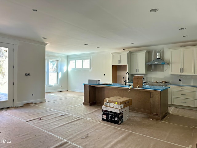 kitchen with sink, ornamental molding, an island with sink, stainless steel gas stovetop, and wall chimney range hood