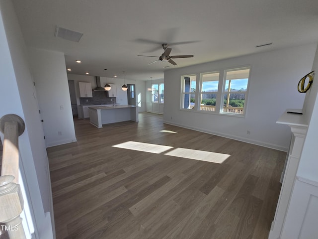 unfurnished living room with ceiling fan, a healthy amount of sunlight, and dark wood-type flooring