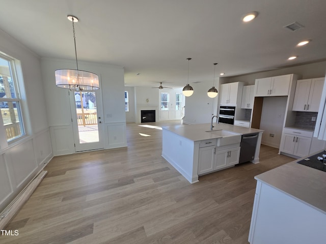 kitchen with white cabinetry, light hardwood / wood-style flooring, pendant lighting, a kitchen island with sink, and black appliances