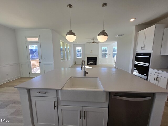 kitchen with dishwasher, an island with sink, white cabinets, and sink