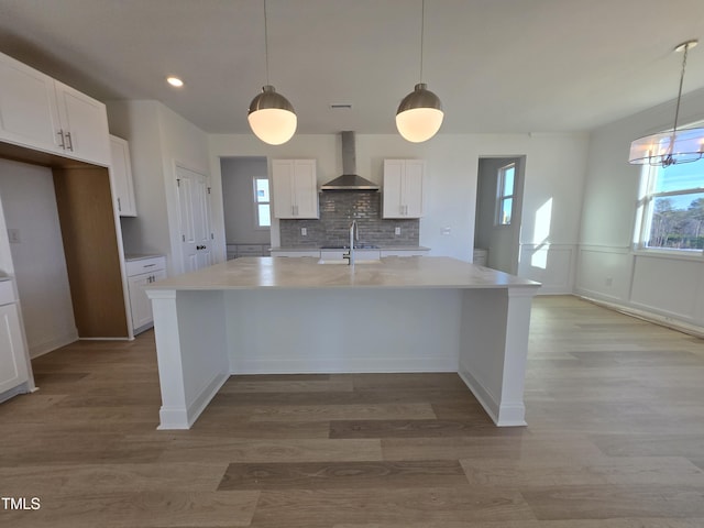 kitchen featuring pendant lighting, a center island with sink, sink, wall chimney exhaust hood, and white cabinetry