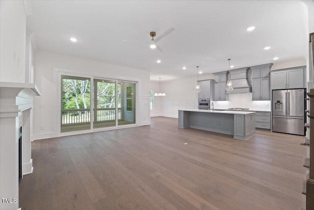 kitchen featuring a kitchen island with sink, premium range hood, hanging light fixtures, gray cabinets, and appliances with stainless steel finishes