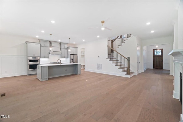 kitchen featuring appliances with stainless steel finishes, light wood-type flooring, a kitchen island with sink, decorative light fixtures, and gray cabinets