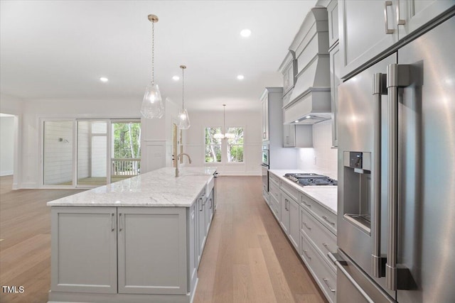 kitchen featuring gray cabinetry, a large island with sink, stainless steel appliances, and hanging light fixtures