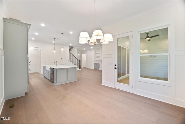 kitchen with gray cabinetry, dishwasher, an island with sink, light hardwood / wood-style floors, and decorative light fixtures