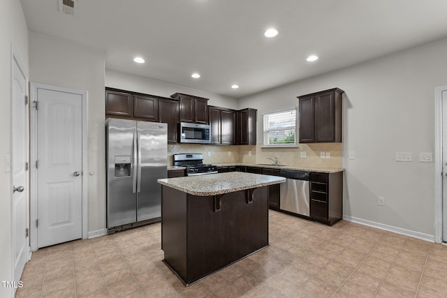 kitchen with a kitchen bar, a center island, stainless steel appliances, light stone countertops, and backsplash