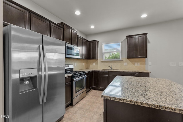 kitchen featuring tasteful backsplash, light stone counters, dark brown cabinetry, and appliances with stainless steel finishes