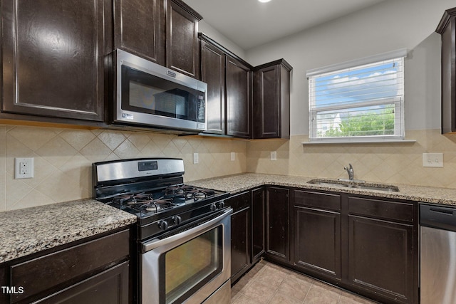 kitchen with appliances with stainless steel finishes, sink, decorative backsplash, dark brown cabinetry, and light stone counters