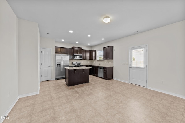 kitchen with appliances with stainless steel finishes, a center island, dark brown cabinets, a sink, and baseboards