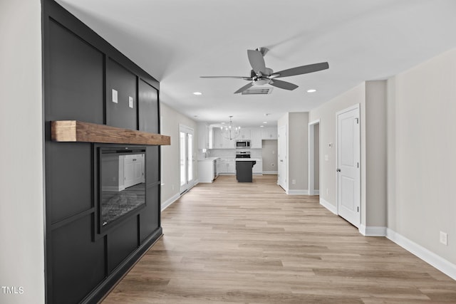 living room with ceiling fan with notable chandelier and light hardwood / wood-style floors