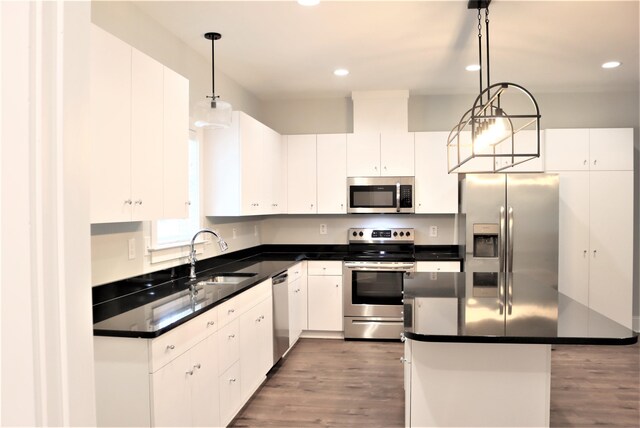 kitchen featuring hanging light fixtures, wood-type flooring, white cabinets, appliances with stainless steel finishes, and sink