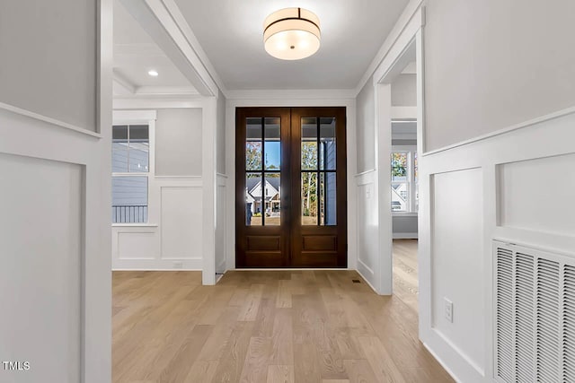 foyer entrance featuring crown molding, french doors, and light wood-type flooring