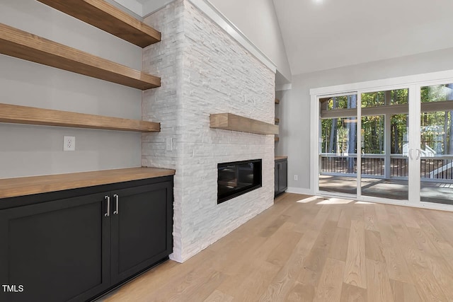 unfurnished living room featuring light hardwood / wood-style floors, a fireplace, and high vaulted ceiling