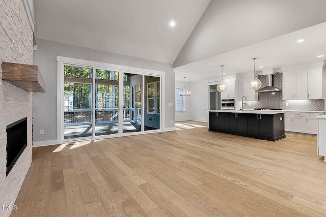 unfurnished living room featuring sink, an inviting chandelier, high vaulted ceiling, light hardwood / wood-style floors, and a fireplace