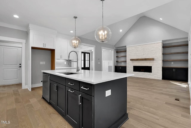 kitchen with pendant lighting, white cabinets, a stone fireplace, sink, and an island with sink