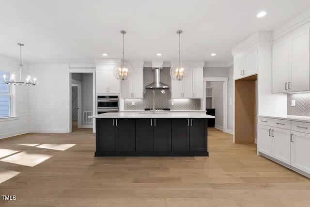 kitchen with pendant lighting, a center island with sink, and wall chimney range hood