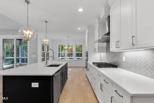 kitchen with sink, an island with sink, decorative light fixtures, and wall chimney range hood