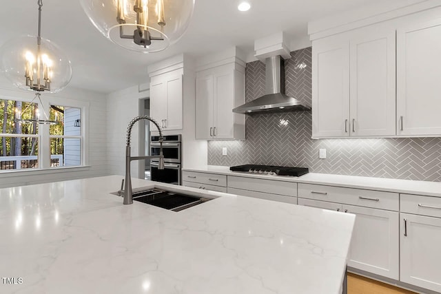 kitchen with light stone countertops, white cabinetry, wall chimney exhaust hood, hanging light fixtures, and gas stovetop