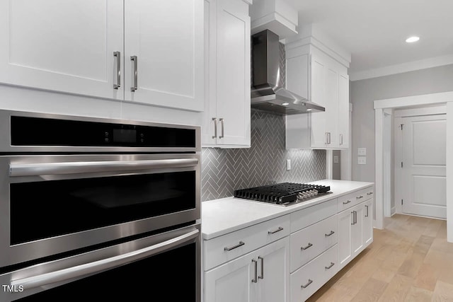 kitchen featuring white cabinets, light hardwood / wood-style floors, wall chimney range hood, and stainless steel gas cooktop