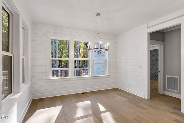 unfurnished dining area featuring wood walls, hardwood / wood-style floors, and a notable chandelier