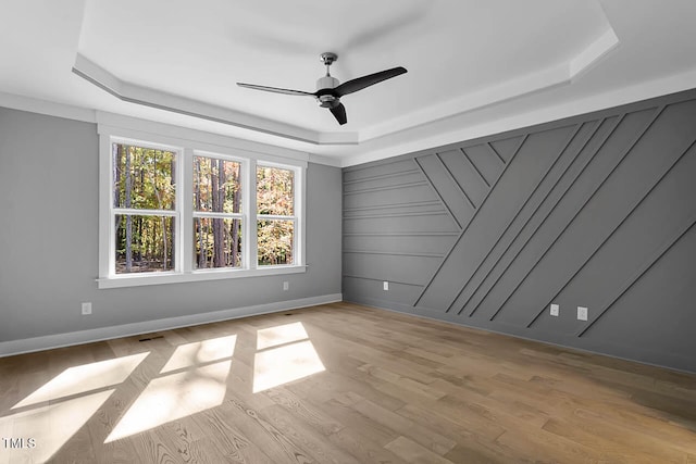 empty room featuring ceiling fan, a raised ceiling, and light hardwood / wood-style flooring