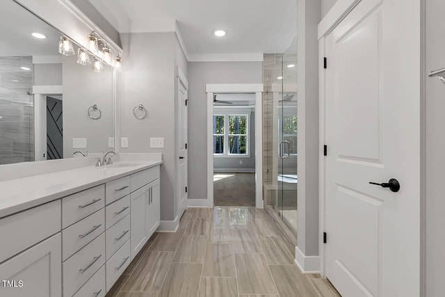 bathroom featuring ceiling fan, vanity, a shower with shower door, and ornamental molding