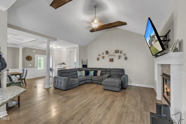 living room featuring lofted ceiling with beams, ceiling fan, a stone fireplace, hardwood / wood-style flooring, and decorative columns