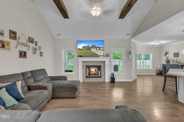 living room featuring wood-type flooring, vaulted ceiling with beams, and a stone fireplace