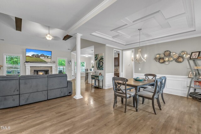 dining space with hardwood / wood-style floors, ceiling fan with notable chandelier, a stone fireplace, and ornate columns