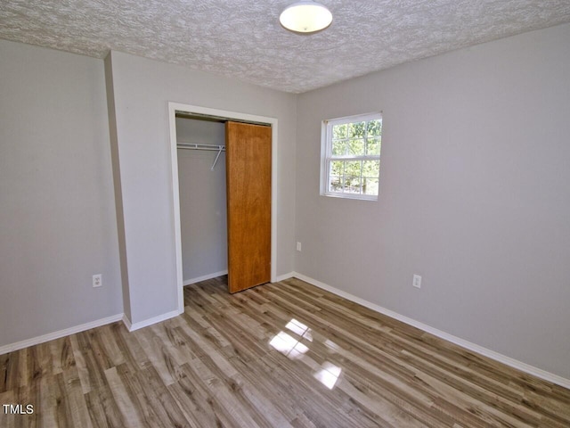 unfurnished bedroom with a textured ceiling, a closet, and hardwood / wood-style floors