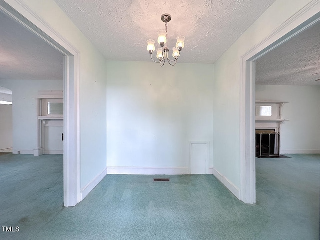 empty room with a textured ceiling, carpet flooring, and an inviting chandelier