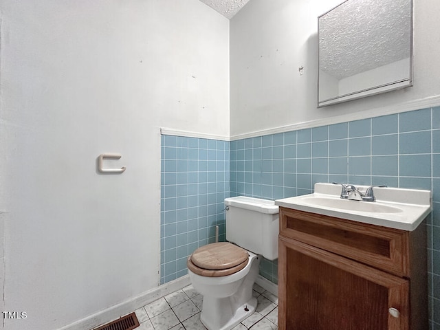 bathroom with a textured ceiling, toilet, tile patterned flooring, tile walls, and vanity