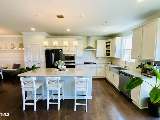 kitchen featuring wall chimney range hood, sink, a center island, black appliances, and decorative light fixtures