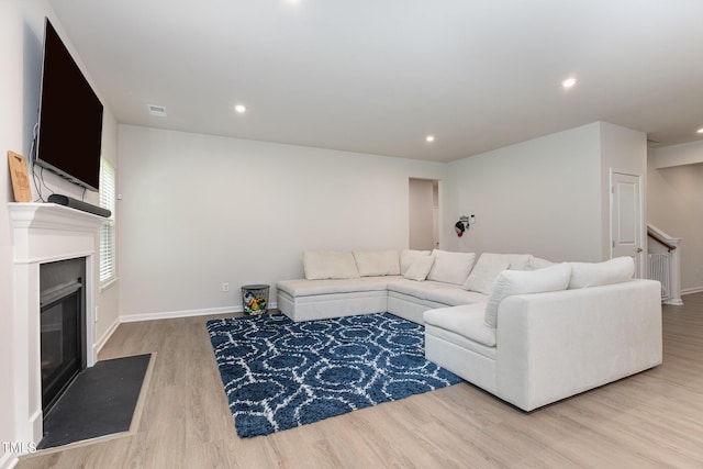 living room featuring recessed lighting, light wood-style floors, a fireplace with flush hearth, baseboards, and stairs