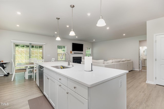 kitchen with an island with sink, a sink, a fireplace, white cabinetry, and stainless steel dishwasher