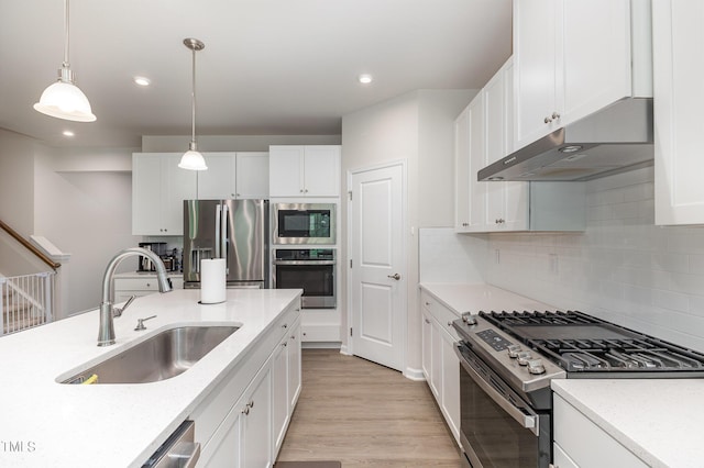 kitchen with light wood-style flooring, appliances with stainless steel finishes, white cabinetry, a sink, and under cabinet range hood