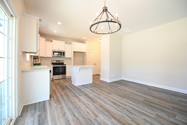 kitchen with white cabinetry, decorative light fixtures, a center island, light wood-type flooring, and appliances with stainless steel finishes