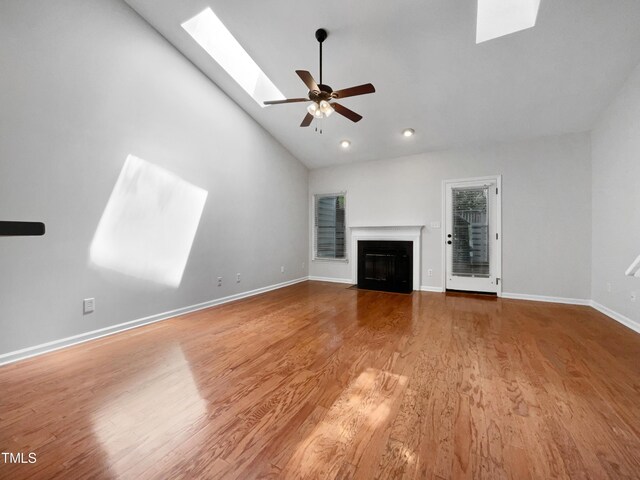 unfurnished living room featuring ceiling fan, hardwood / wood-style flooring, a skylight, and high vaulted ceiling