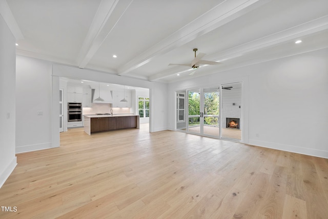 unfurnished living room featuring light wood-type flooring, beamed ceiling, ceiling fan, sink, and a fireplace