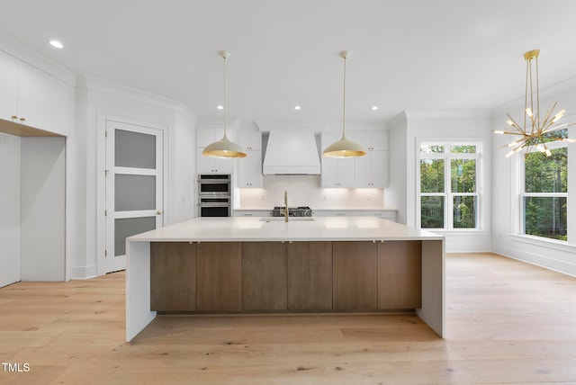 kitchen featuring white cabinets, custom exhaust hood, hanging light fixtures, light hardwood / wood-style flooring, and stainless steel double oven