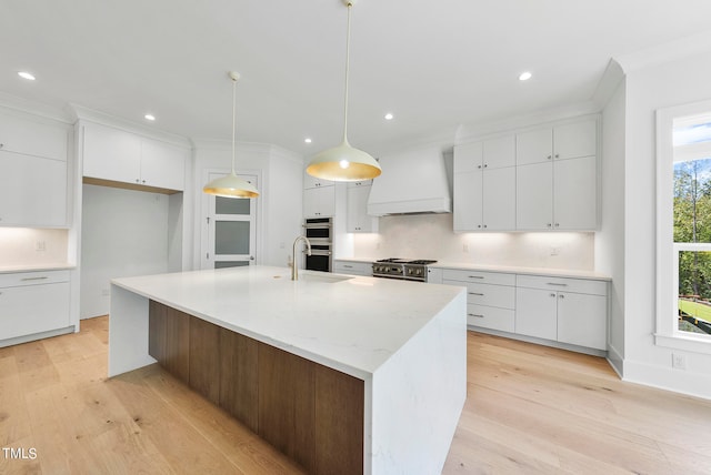 kitchen with a center island with sink, premium range hood, a wealth of natural light, and white cabinetry