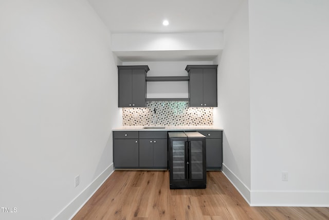 kitchen with gray cabinets, tasteful backsplash, light hardwood / wood-style flooring, wine cooler, and sink