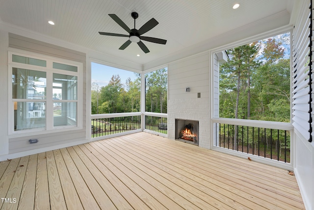 unfurnished sunroom with a healthy amount of sunlight, ceiling fan, and a fireplace