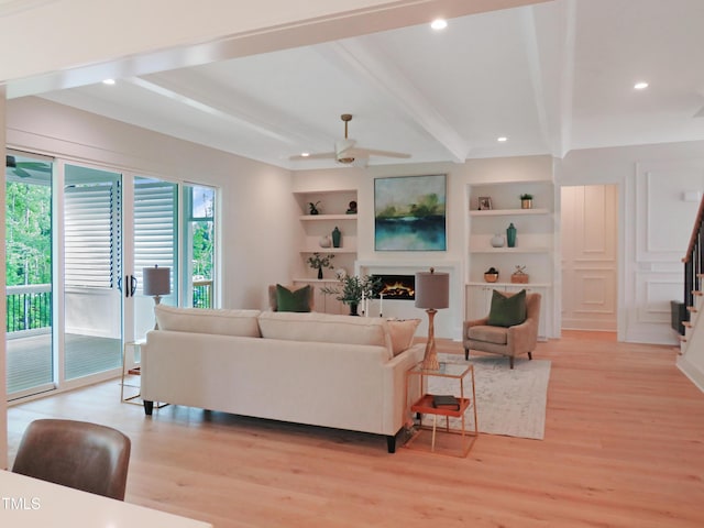 2506 Silas Peak Ln, Apex, NC 27523 - living area with light wood finished floors, beamed ceiling, stairs, ceiling fan, and a warm lit fireplace