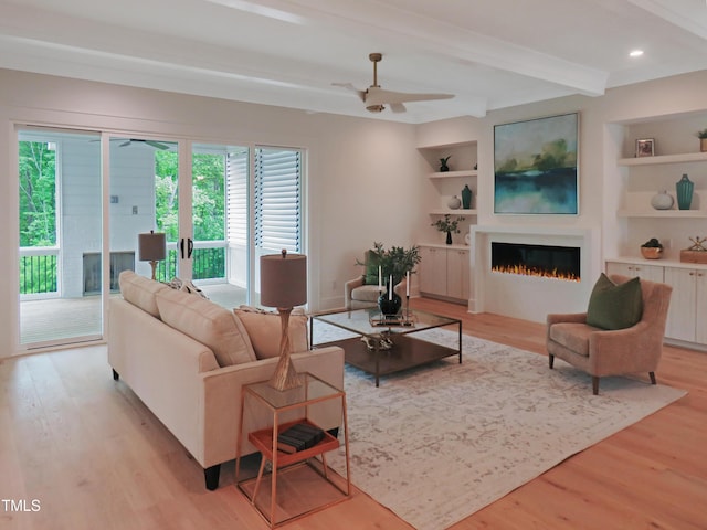 2506 Silas Peak Ln, Apex, NC 27523 - living room featuring light wood finished floors, beam ceiling, a lit fireplace, ceiling fan, and built in shelves