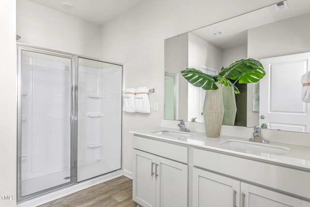 bathroom featuring hardwood / wood-style floors, dual vanity, and a shower with shower door