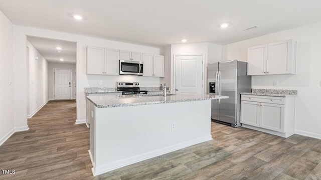 kitchen with wood finished floors, a center island with sink, recessed lighting, a sink, and appliances with stainless steel finishes